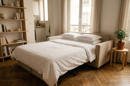 Canapé convertible déplié en lit dans un petit studio parisien avec parquet en chevron et bibliothèque en bois